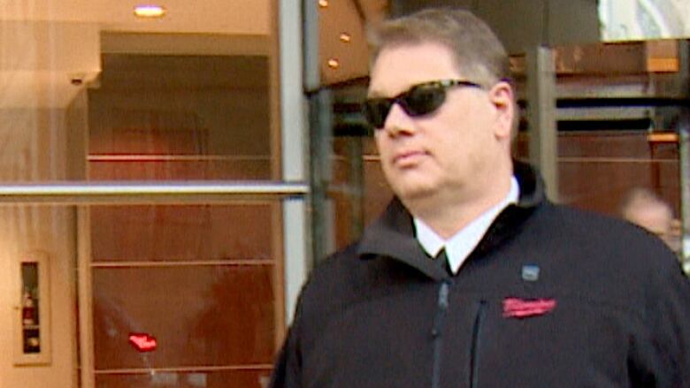 A man in sunglasses and a black coat walks out of the Calgary courthouse. 