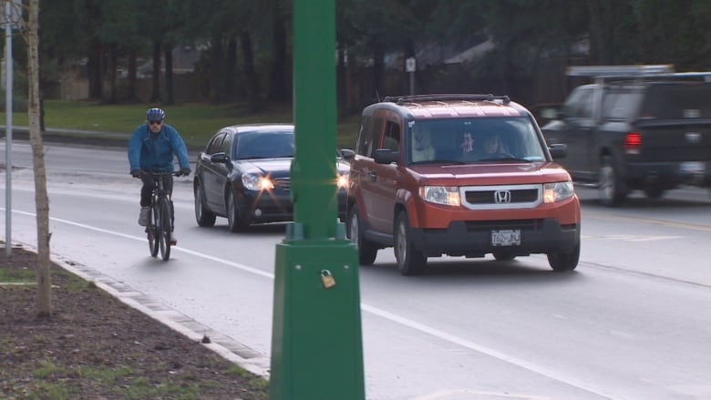 A cyclist in blue jacket rides in a bike lane without any barriers next to traffic