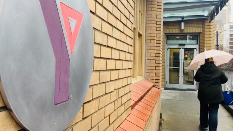 A woman carrying an umbrella walks towards the door of a brick building