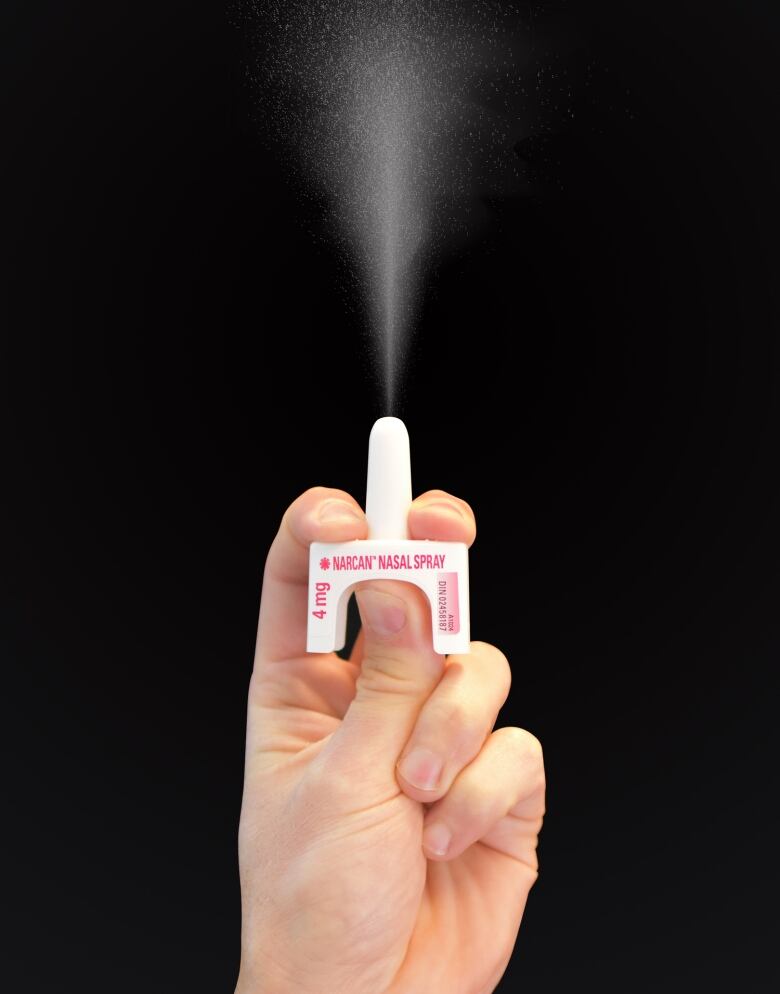 A person's left hand holding a dose of Narcan and dispensing the nasal spray into the air to demonstrate how it's used in a person's nose.