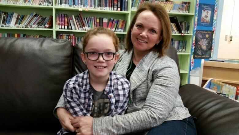 A file photo from 2018 of a blond woman in a book-lined room embracing a young girl. 