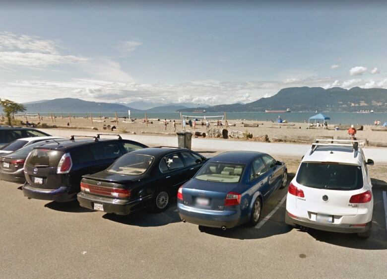 Vehicles are parked in a row in front of a sandy beach.