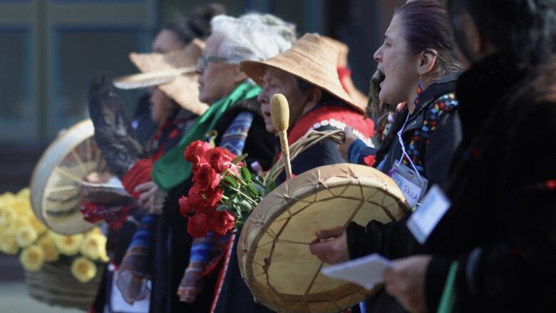 Indigenous people bang on drums while singing.