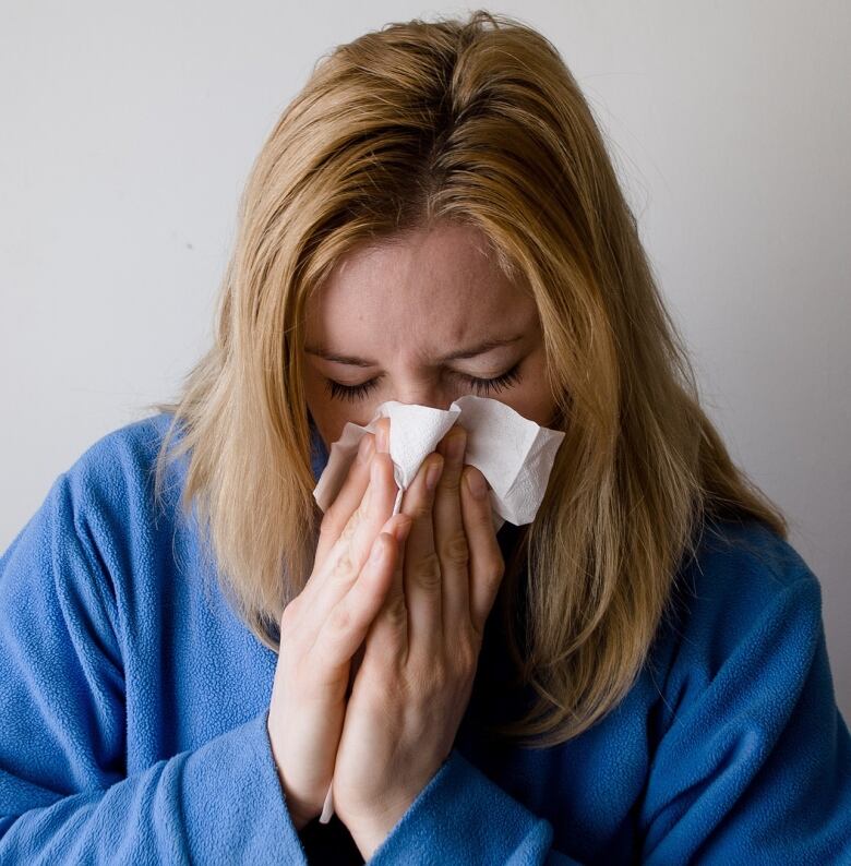 Woman sneezing and using a tissue.