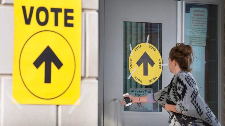 A woman opens a door with a sign that says VOTE with an arrow pointing inside