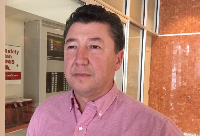 An Indigenous man with short hair is seen wearing a pink button up shirt.