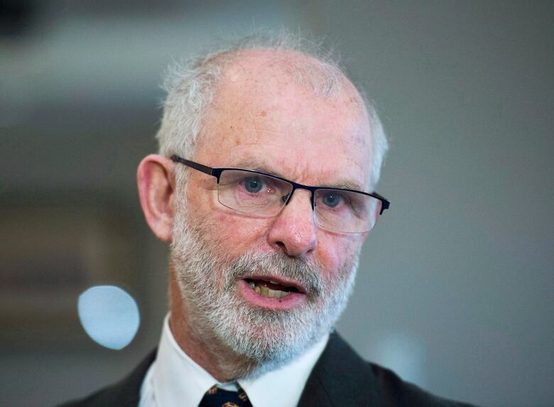 A closeup photo of a bald man with glasses and a beard.