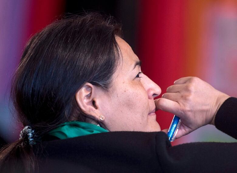 A closeup shows a woman with a long dark hair looking to the side as she listens, with a hand holding a pen raised to her face.