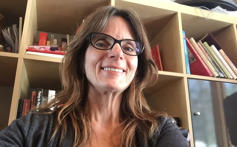 A woman sitting in front of a bookshelf smiles at the camera.