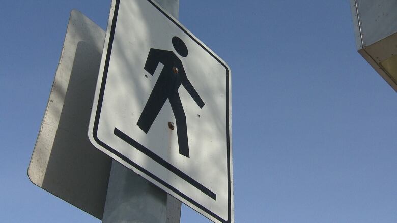 A closeup shows a crosswalk sign against a blue sky.