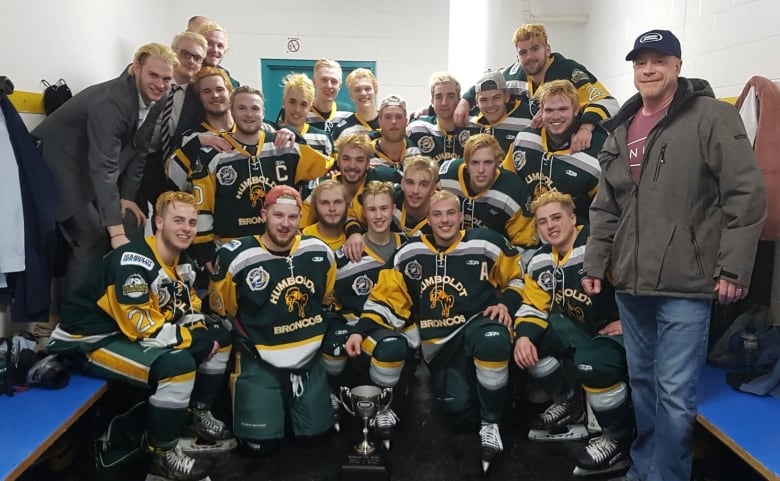 A team of hockey players and coaches huddle together for a photo.