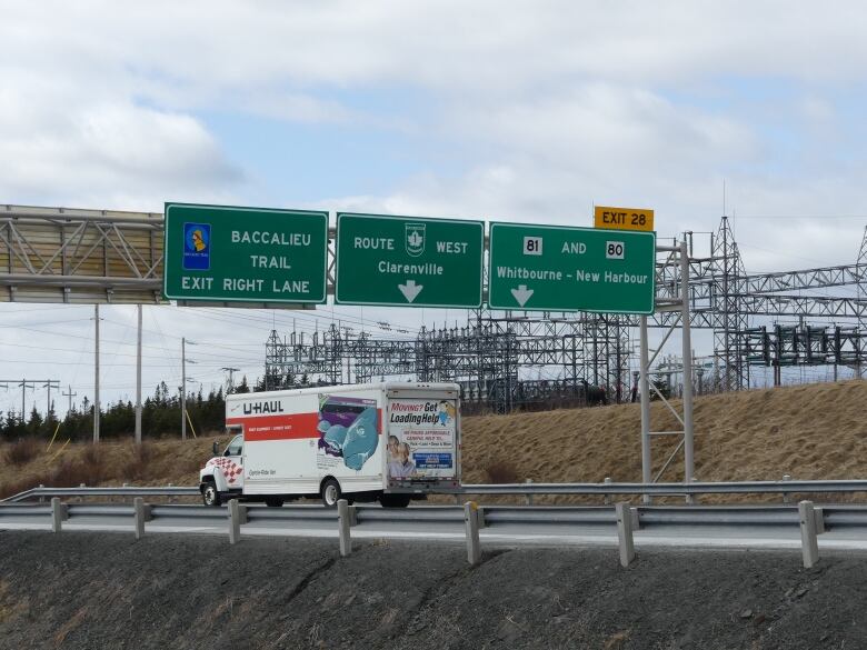 Signs above a highway point to Clarenville, Whitbourne-New Harbour and the Baccalieu Trail. A Uhaul truck is driving on the highway.