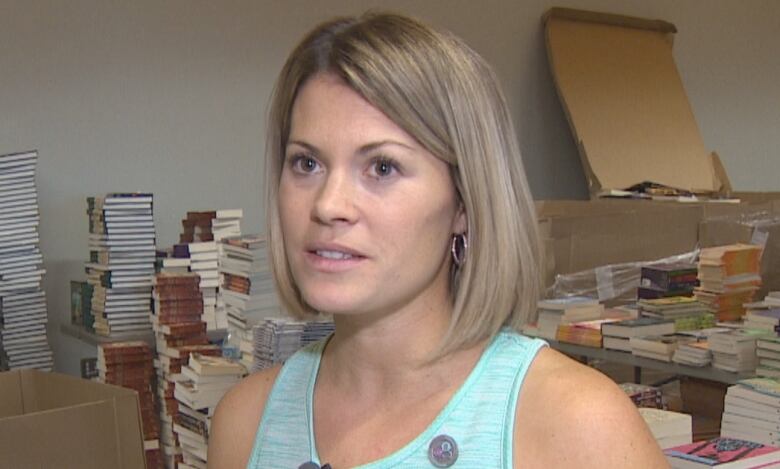 A woman wearing a blue tank top with piles of books behind her