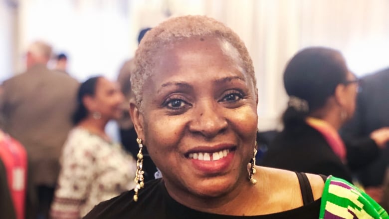 A Black woman with a short hair cut smiles at the camera among a crowd.