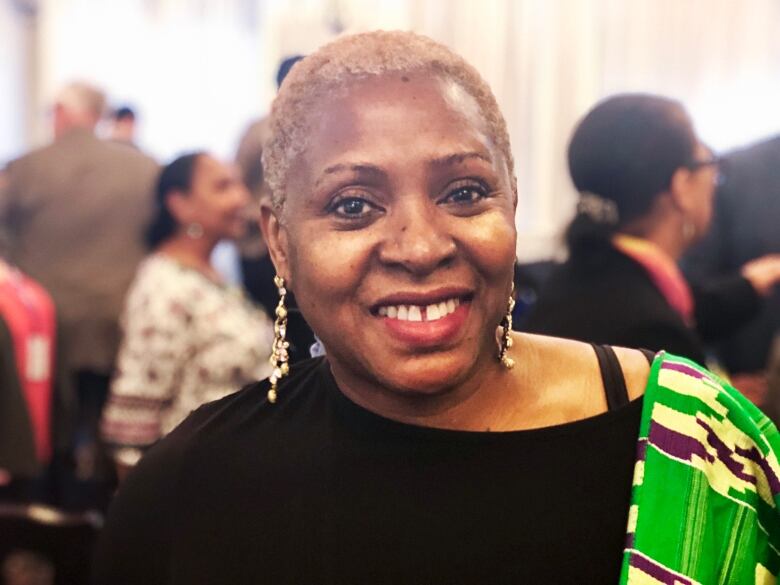 A Black woman with a short hair cut smiles at the camera among a crowd.