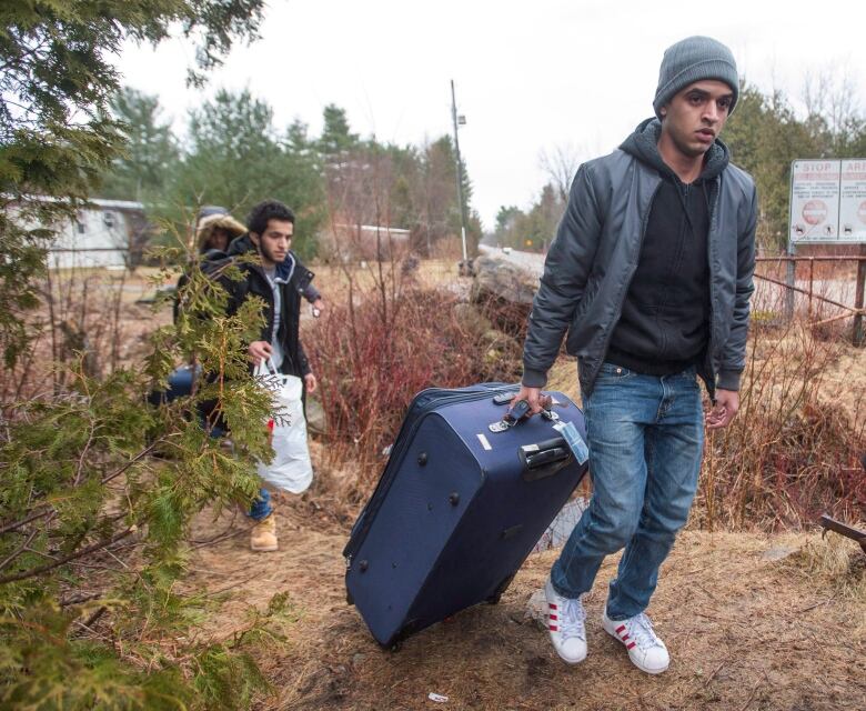 Two people carry bags next to a road.