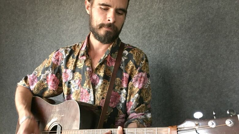 A man in a colourful shirt plays a guitar