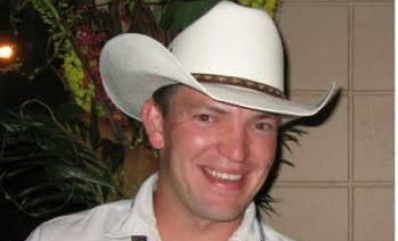 Young man wears white cowboy hat and smiles.