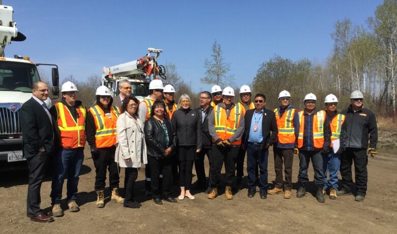 18 people stand in a row.  Most are in hi-viz vests and hard hats.  Margaret, Patty Hajdu and Alvin Fiddler are near the middle of the group.