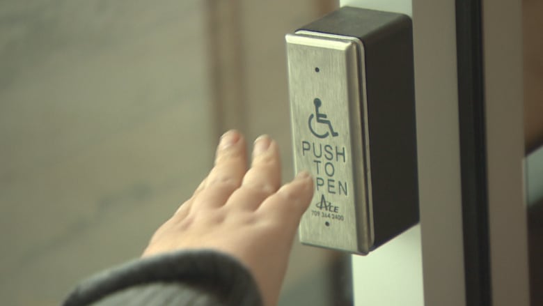 a person's hand  reaches toward a push to open button at a doorway