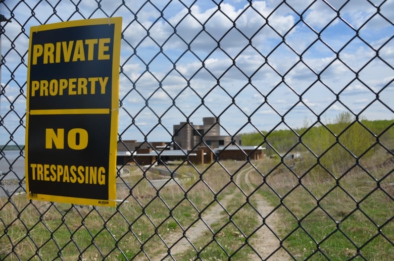 A 'private property/no trespassing sign' on a chain link fence with a large house in the background  