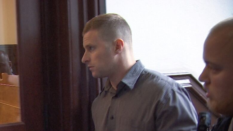 A white man with short brown hair is seen in profile wearing a stripped button up shirt