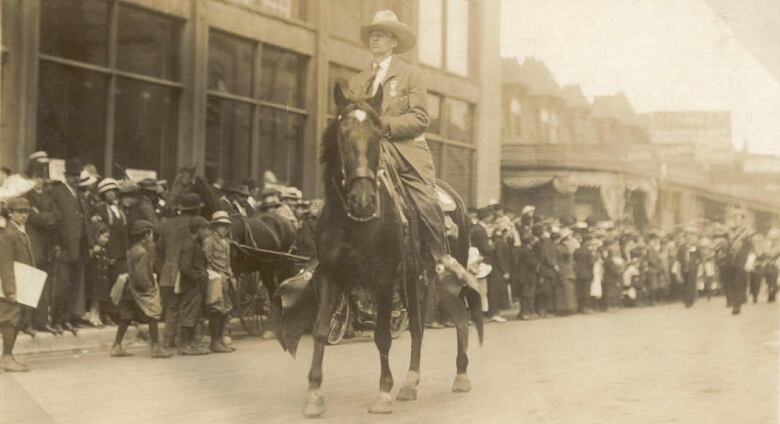 A man rides a horse down a street lined with spectators.