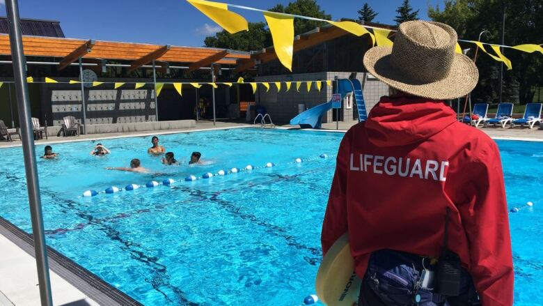 Lifeguard in red watches swimmers in a pool.