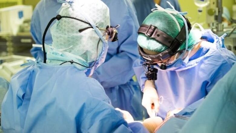 Three surgeons are seen in full gear operating on an unseen patient.