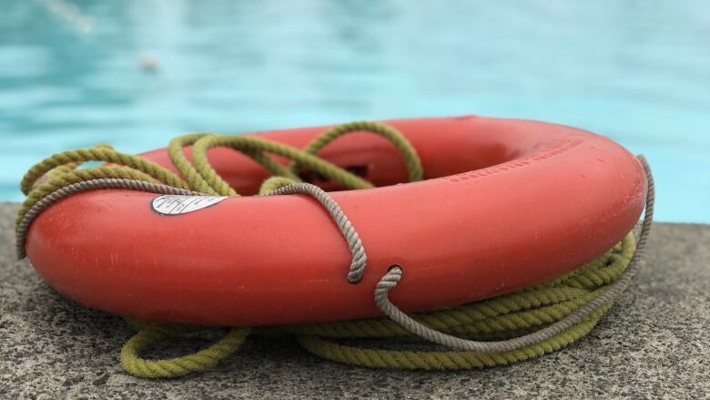 A red lifeguard flotation device ring is pictured at the edge of a pool.