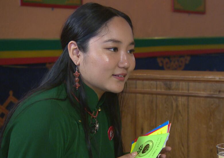 A Tibetan woman wears a green shirt and holds colourful paper in her hands.