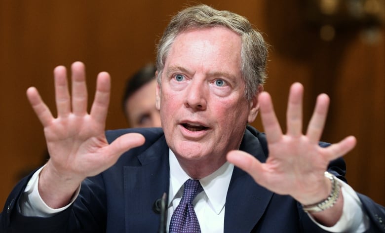 A man in a suit gestures while speaking -- splaying the fingers on both his hands.