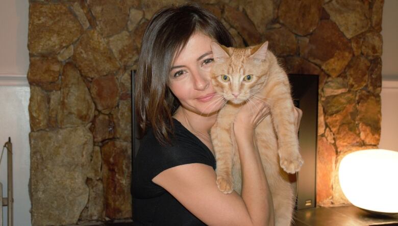 Rebeka Breder holds up an orange tabby cat.