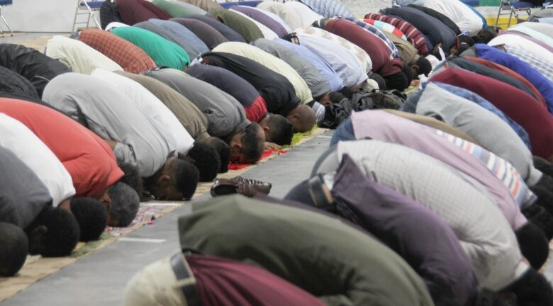 Men kneel and bend their heads to the floor in prayer