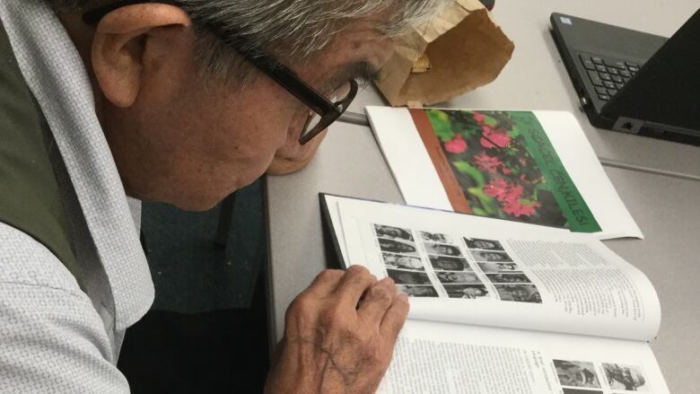 A man with grey hair and black-framed glasses consults a thick book.