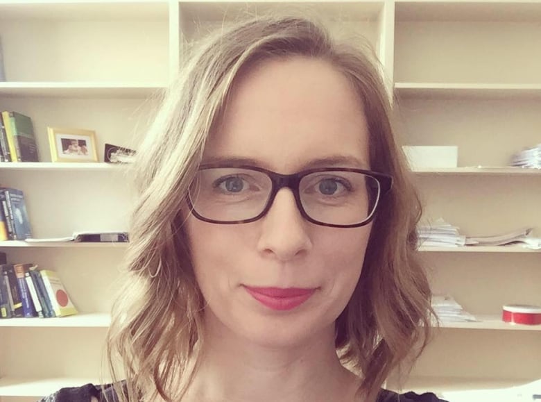 A woman wearing glasses poses in front of a bookshelf.