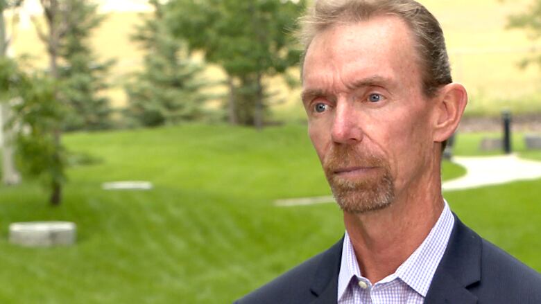 A man with short hair is pictured on a golf course. He looks past the camera.