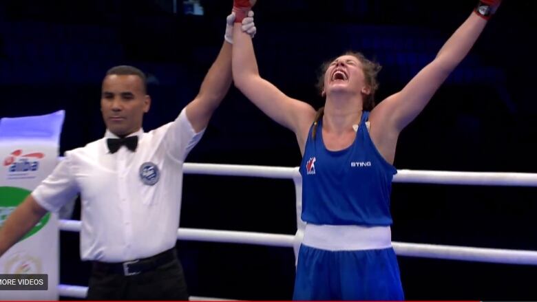 A referee holding up the arm of a girl wearing a blue boxing outfit