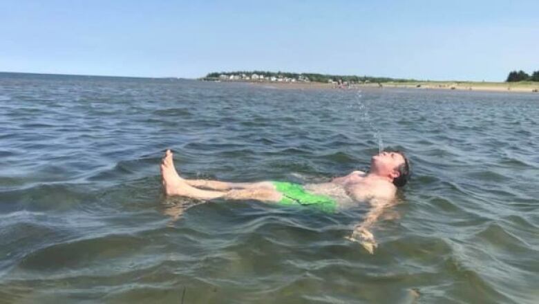 A man in bright green swimming trunks floats on his back, with water spouting from his mouth.