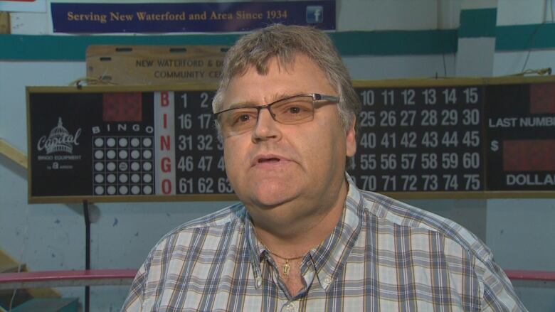 A man in a plaid shirt and glasses speaks to someone off camera.