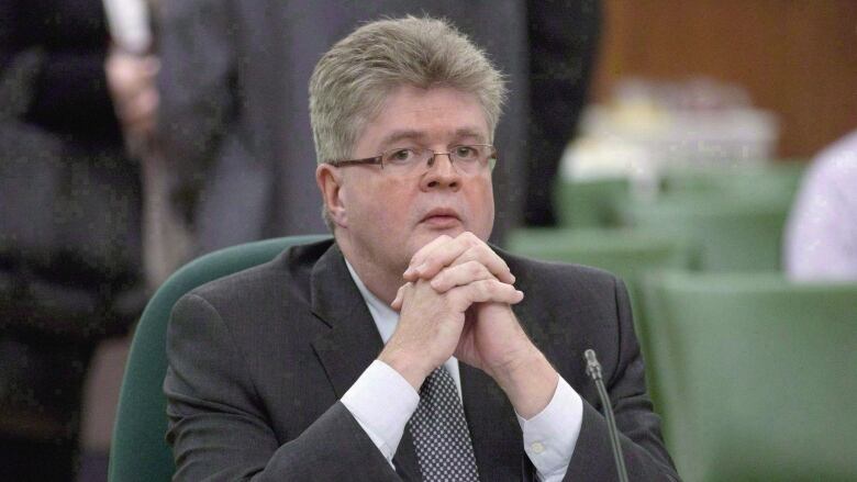 A man in a suit sits with his hands held under his chin. 