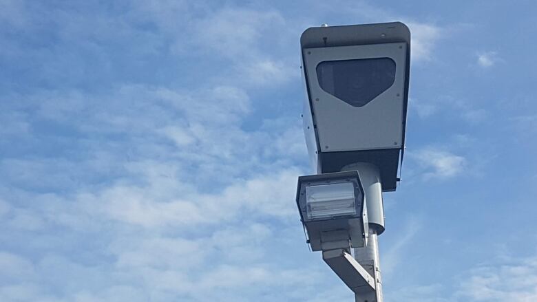 A boxy speed camera. Blue sky with some clouds in the background. 