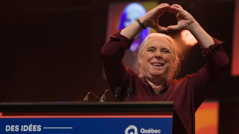 A woman holds up a heart symbol with her hands. 