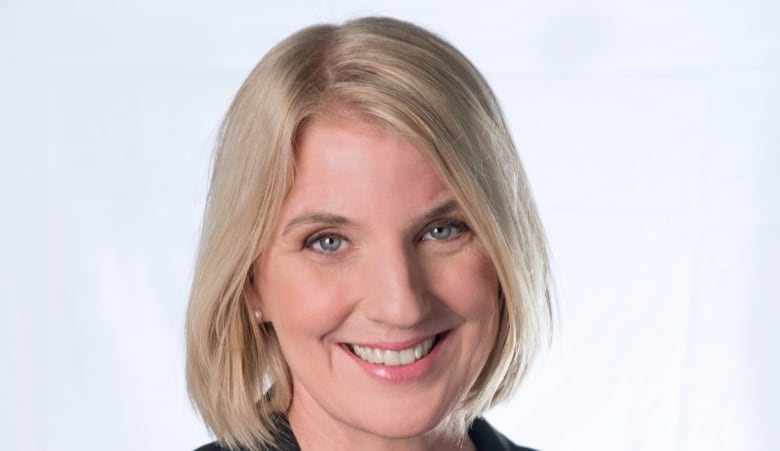 Blonde woman in black jacket smiles to camera.