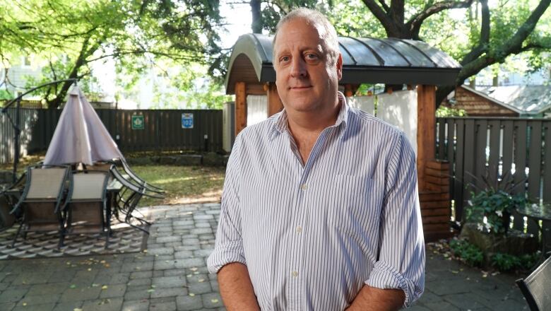 A man in shirtsleeves stands in a garden.