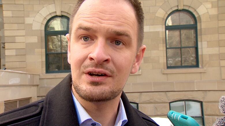 A bald man with a goatee is seen in front of the legislative building.