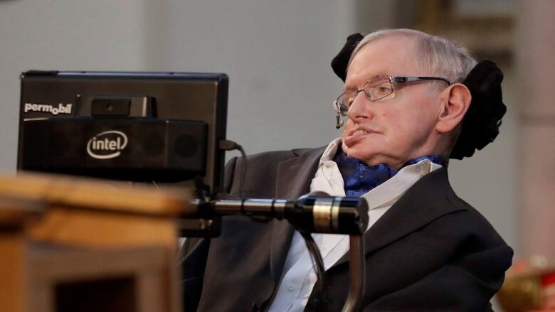 Stephen Hawking is seated in his wheelchair in front of a podium.