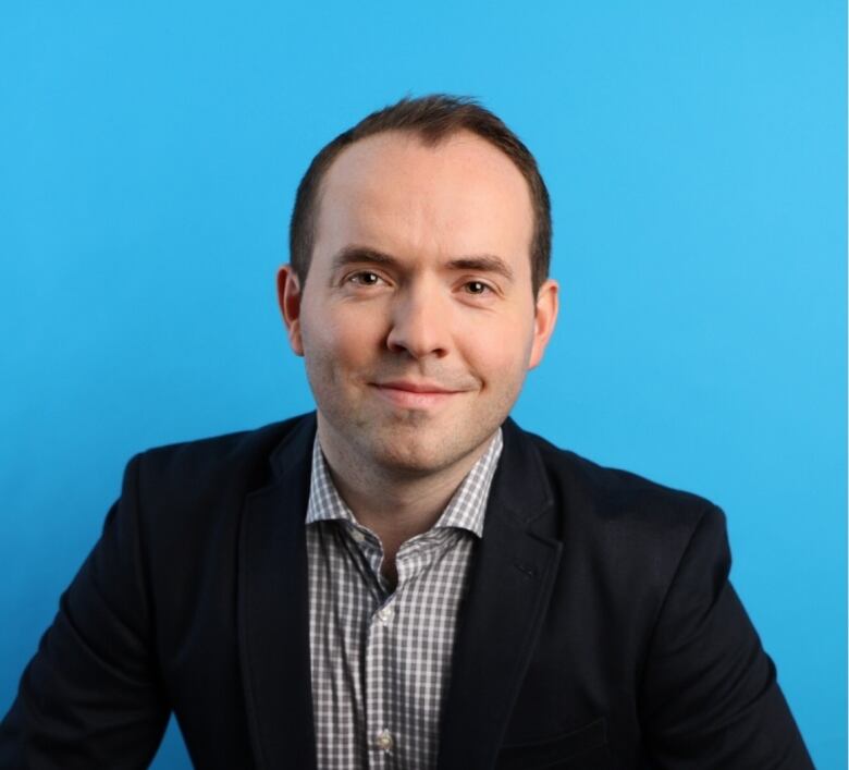 A man poses in front of a bright blue background