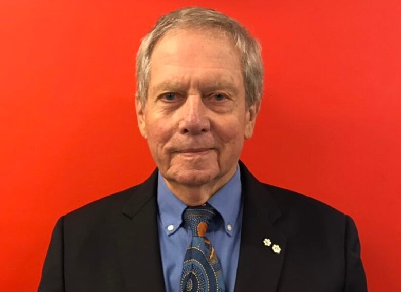 A man stands against a bright red background