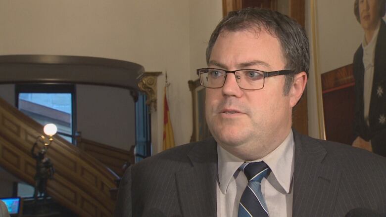 A man in glasses and a suit responds to a question off camera inside the halls of the legislature.